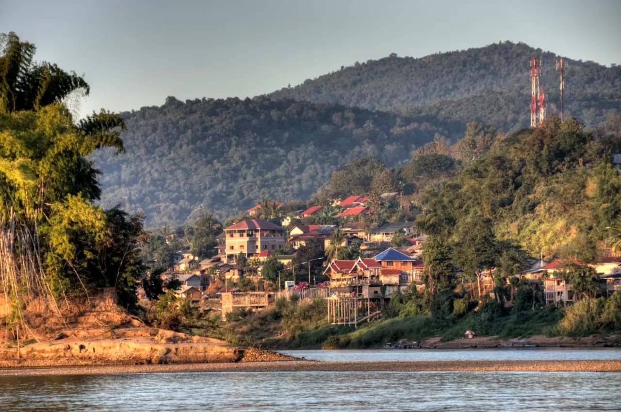 Houayxay seen from the Mekong: red-roofed houses on the riverbank below forested hills