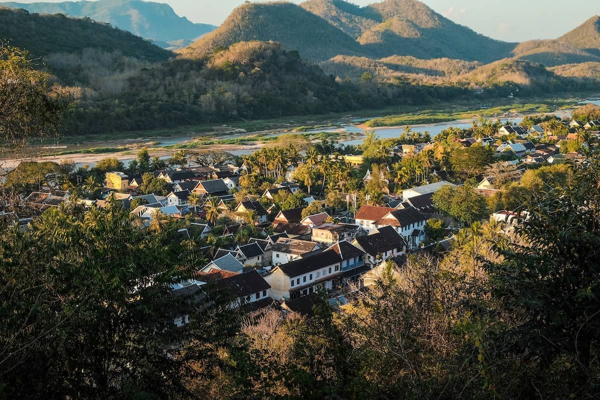Luang Prabang seen from above, its roofs among palm trees with the Mekong and the hills behind