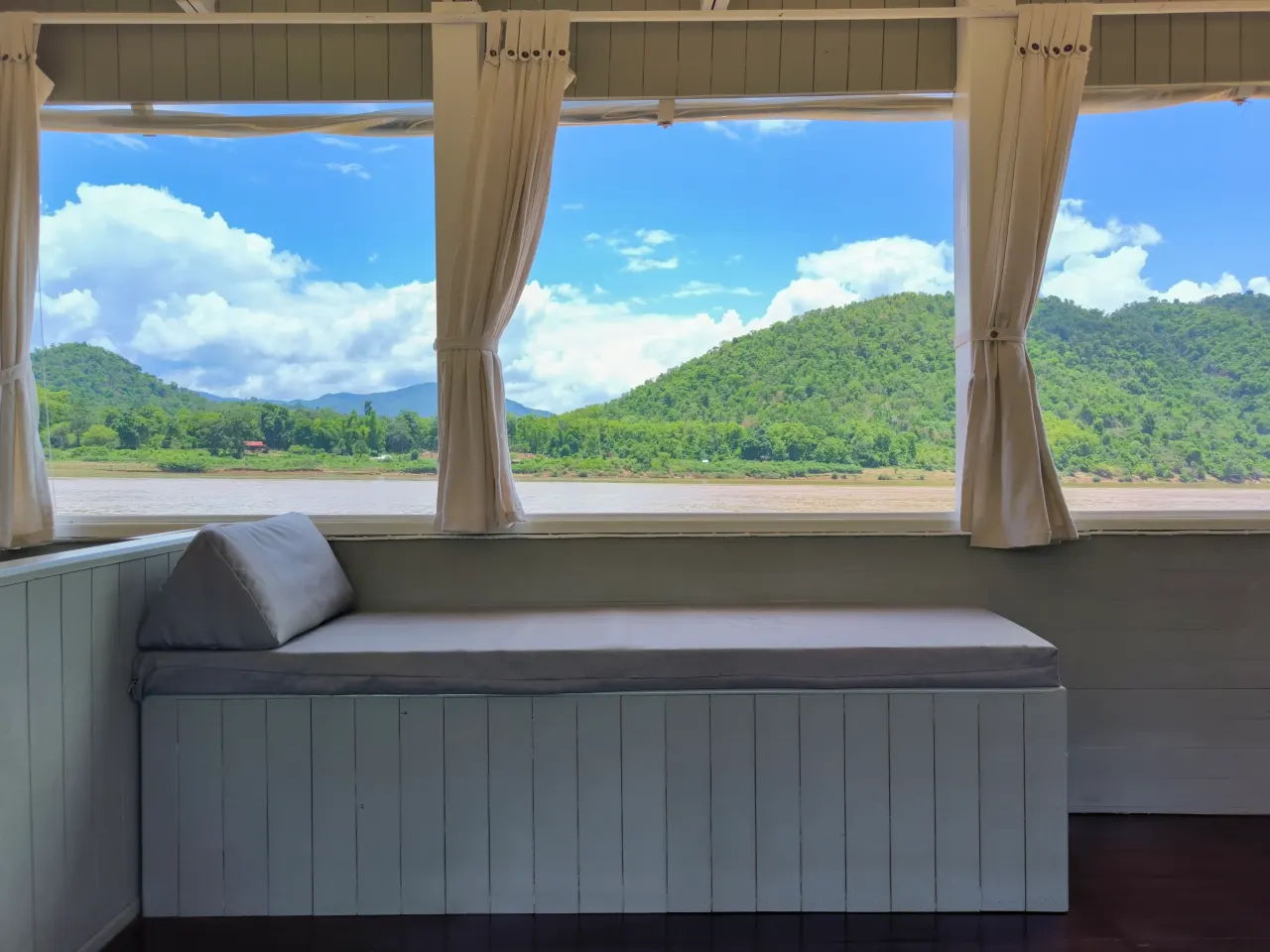 Window seat on the Mekong Cruises boat overlooking forested mountains of Laos